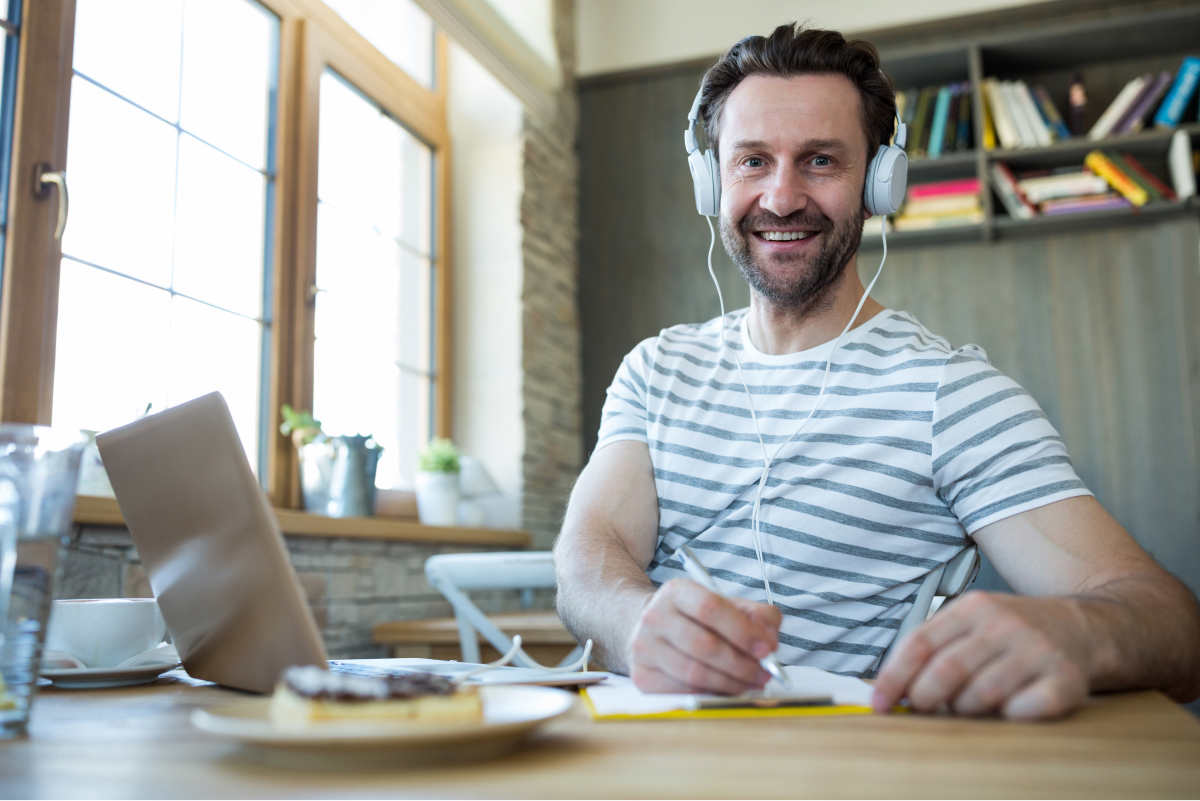smiling-man-with-headphones-writing-his-diary-coffee-shop 1
