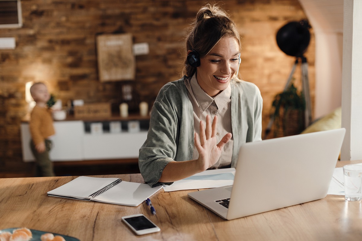happy-female-entrepreneur-waving-video-call-laptop-home 1