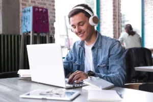teenage-student-headphones-sitting-table-typing-notebook 1